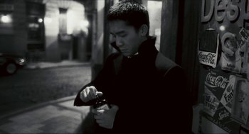 Movie still from “Happy Together” (1997), directed by Kar-Wai Wong – A man looking at his watch while holding a cell phone; Medium shot, Low angle