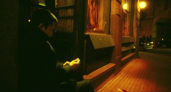 Movie still from “Happy Together” (1997), directed by Kar-Wai Wong – A man sitting on a bench on the side of a building; Wide shot, High angle