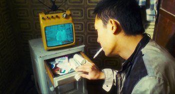 Movie still from “Happy Together” (1997), directed by Kar-Wai Wong – A man smoking a cigarette in front of a television; Close Up shot, Over the shoulder angle