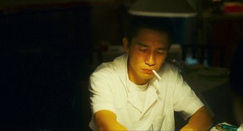 Movie still from “Happy Together” (1997), directed by Kar-Wai Wong – A man sitting at a table with a cigarette in his mouth; Close Up shot, High angle