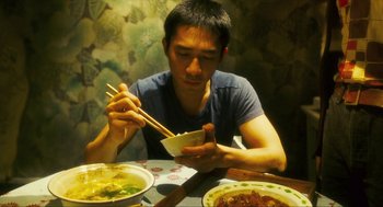 Movie still from “Happy Together” (1997), directed by Kar-Wai Wong – A man sitting at a table with chopsticks in a bowl; Medium shot, High angle