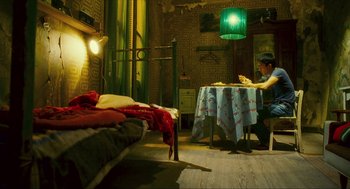 Movie still from “Happy Together” (1997), directed by Kar-Wai Wong – A person sitting at a table in a room with two beds; Wide shot, High angle