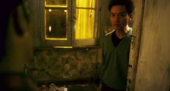 Movie still from “Happy Together” (1997), directed by Kar-Wai Wong – A young man standing in a room next to an open window; Medium shot, High angle