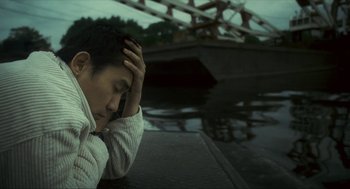 Movie still from “Happy Together” (1997), directed by Kar-Wai Wong – A man sitting on the side of a river with his head on his hand; Close Up shot, High angle