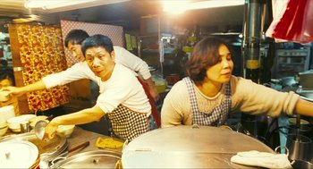 Movie still from “Happy Together” (1997), directed by Kar-Wai Wong – A group of people standing in a kitchen preparing food; Medium shot, High angle