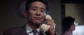 An older man in a suit holding a phone to his ear