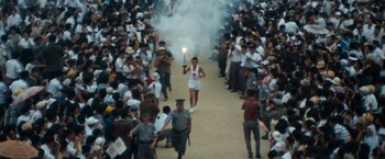 A woman walking down a street holding a torch in front of a crowd of onlookers
