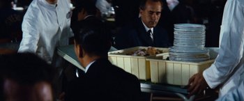 Movie still from “Tokyo Olympiad” (1965), directed by Kon Ichikawa – A man sitting at a table in front of a tray of food; Medium shot, Over the shoulder angle