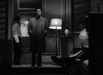 A black and white photo of a man standing in front of a lamp