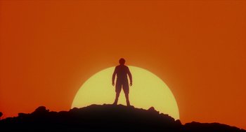 Movie still from “Tommy” (1975), directed by Ken Russell – A man standing on top of a hill in front of the sun; Wide shot, Low angle