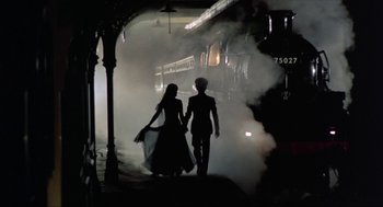 Movie still from “Tommy” (1975), directed by Ken Russell – A man and a woman walking through a train station; Wide shot, Low angle