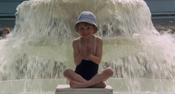 Movie still from “Tommy” (1975), directed by Ken Russell – A little boy sitting in front of a waterfall; Wide shot, High angle