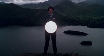 Movie still from “Tommy” (1975), directed by Ken Russell – A man standing on top of a hill holding a white object; Wide shot, Low angle