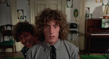 Movie still from “Tommy” (1975), directed by Ken Russell – A young man with long curly hair wearing a shirt and a tie; Close Up shot, Over the shoulder angle