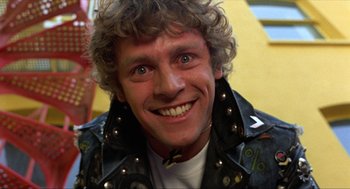Movie still from “Tommy” (1975), directed by Ken Russell – A person wearing a leather jacket smiling; Close Up shot, Low angle