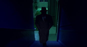 Movie still from “Tommy” (1975), directed by Ken Russell – A man in a suit and a hat standing in a dark room; Wide shot, Low angle