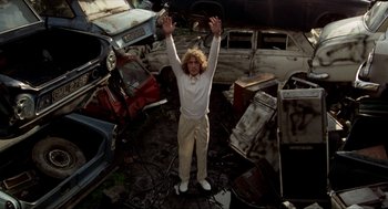 Movie still from “Tommy” (1975), directed by Ken Russell – A man standing in front of a pile of junk; Wide shot, Low angle