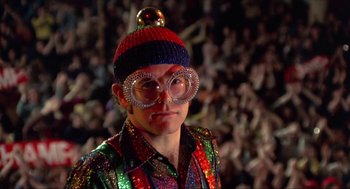 Movie still from “Tommy” (1975), directed by Ken Russell – A man wearing a hat and glasses in front of a crowd; Close Up shot, Low angle