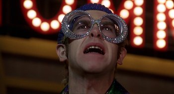 Movie still from “Tommy” (1975), directed by Ken Russell – A man wearing a pair of glasses and a hat; Close Up shot, Low angle