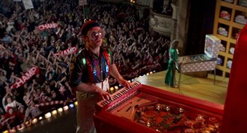 Movie still from “Tommy” (1975), directed by Ken Russell – A man in a clown costume playing a piano; Wide shot, High angle