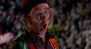 Movie still from “Tommy” (1975), directed by Ken Russell – A man wearing glasses and wearing a colorful shirt; Close Up shot, Low angle