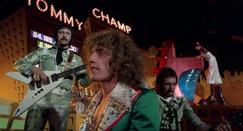 Movie still from “Tommy” (1975), directed by Ken Russell – A group of people that are standing in a room; Medium shot, Low angle