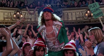 Movie still from “Tommy” (1975), directed by Ken Russell – A man in a green jacket and a red and white striped hat; Medium shot, Low angle