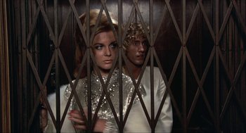 Movie still from “Tommy” (1975), directed by Ken Russell – A man and a woman standing behind a metal gate; Medium shot, Low angle