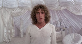 Movie still from “Tommy” (1975), directed by Ken Russell – A man in a white shirt is standing in front of a tent; Medium shot, Low angle