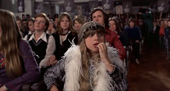 Movie still from “Tommy” (1975), directed by Ken Russell – A woman in a crowd of people sitting in front of a wall; Medium shot, High angle