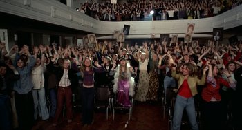 Movie still from “Tommy” (1975), directed by Ken Russell – A group of people sitting in chairs in front of a crowd; Wide shot, High angle
