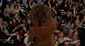 Movie still from “Tommy” (1975), directed by Ken Russell – A group of people in a room with a person on a guitar; Wide shot, High angle