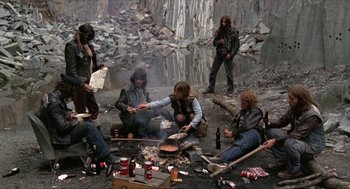 Movie still from “Tommy” (1975), directed by Ken Russell – A group of people sitting around a campfire; Wide shot, High angle