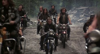Movie still from “Tommy” (1975), directed by Ken Russell – A group of people riding motorcycles down a dirt road; Wide shot, High angle