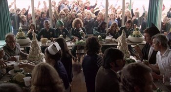 Movie still from “Tommy” (1975), directed by Ken Russell – A group of people sitting at a table with food on top of it; Wide shot, High angle