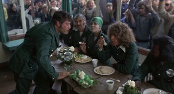 Movie still from “Tommy” (1975), directed by Ken Russell – A group of people sitting around a table eating food; Medium shot, Over the shoulder angle