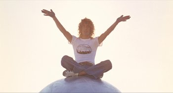 Movie still from “Tommy” (1975), directed by Ken Russell – A man sitting on top of a globe with his arms outstretched; Medium shot, Low angle