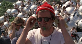 Movie still from “Tommy” (1975), directed by Ken Russell – A man wearing a red and white hat while holding his hands to his ears; Medium shot, High angle