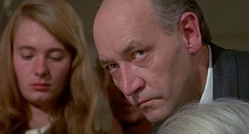 Movie still from “Topaz” (1969), directed by Alfred Hitchcock – A man with a bald head looking at the camera; Close Up shot, Over the shoulder angle