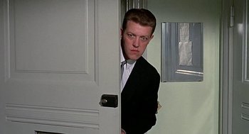 Movie still from “Topaz” (1969), directed by Alfred Hitchcock – A man in a suit and tie standing in front of an open door; Close Up shot, Over the shoulder angle