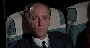 Movie still from “Topaz” (1969), directed by Alfred Hitchcock – A man in a suit and tie sitting in an airplane seat; Close Up shot, Over the shoulder angle