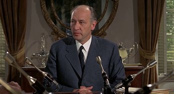 Movie still from “Topaz” (1969), directed by Alfred Hitchcock – A man wearing a suit and tie sitting in front of microphones; Close Up shot, Low angle