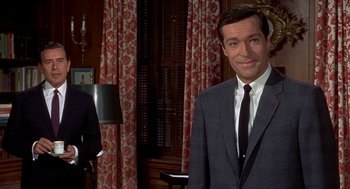 Movie still from “Topaz” (1969), directed by Alfred Hitchcock – A man wearing a suit and tie standing in front of a curtain; Medium shot, Over the shoulder angle