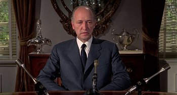 Movie still from “Topaz” (1969), directed by Alfred Hitchcock – A man wearing a suit and tie sitting at a table; Close Up shot, Low angle