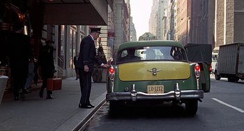 Movie still from “Topaz” (1969), directed by Alfred Hitchcock – A man standing next to a green and yellow car on the side of the road; Wide shot, Low angle