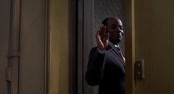 Movie still from “Topaz” (1969), directed by Alfred Hitchcock – A man in a suit and tie holding his hand up; Medium shot, Low angle