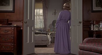 Movie still from “Topaz” (1969), directed by Alfred Hitchcock – A woman in a purple dress standing in front of a bed; Wide shot, Over the shoulder angle
