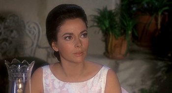 Movie still from “Topaz” (1969), directed by Alfred Hitchcock – A beautiful woman in a white dress sitting in front of a plant; Close Up shot, Over the shoulder angle