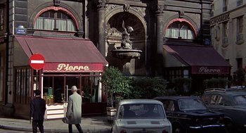 Movie still from “Topaz” (1969), directed by Alfred Hitchcock – A man walking down the street in front of a building; Wide shot, Over the shoulder angle