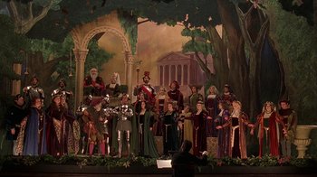 Movie still from “Topsy-Turvy” (1999), directed by Mike Leigh – A group of people dressed in medieval costumes on a stage; Extreme Wide shot, High angle